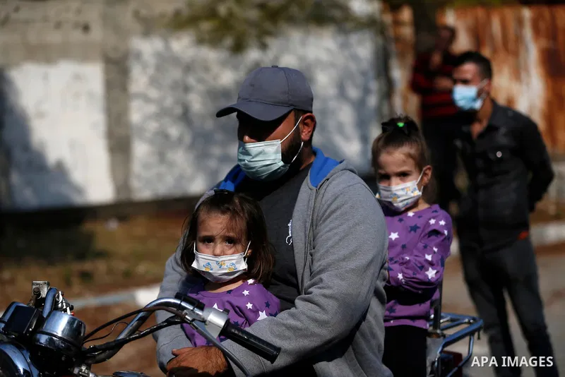 A Palestinian man wearing a mask, rides a motorcycle with his children, on a street in Gaza City on November 8, 2020. Photo by Osama Baba