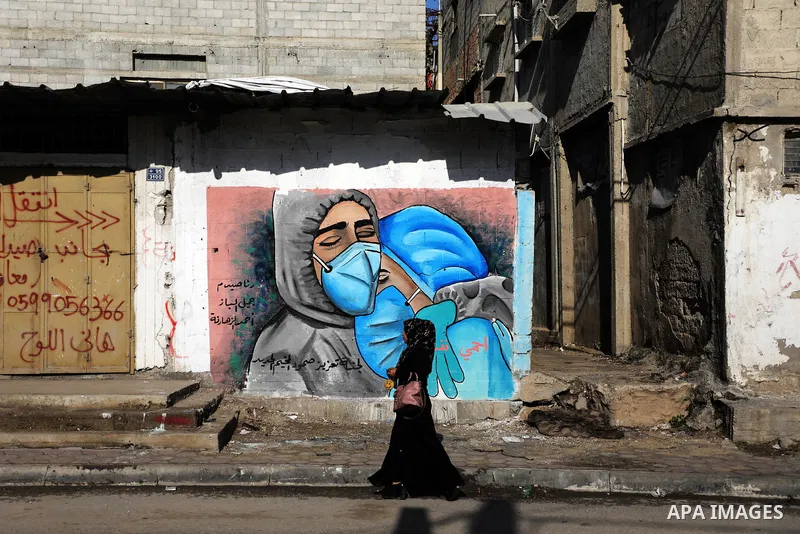 A Palestinian women walks past a mural, showing doctors mask-clad due to the COVID-19 coronavirus pandemic, in the Nusseirat refugee camp in the central Gaza Strip on November 16, 2020. Photo by Ashraf Amra