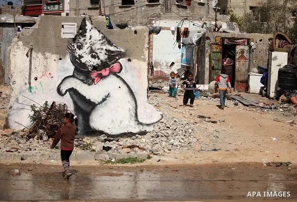 A Palestinian girl walks in front of a mural of a kitten, said to have been painted by British street artist Banksy, on the remains of a house that was destroyed during the 50-day war between Israel and Hamas militants i...
