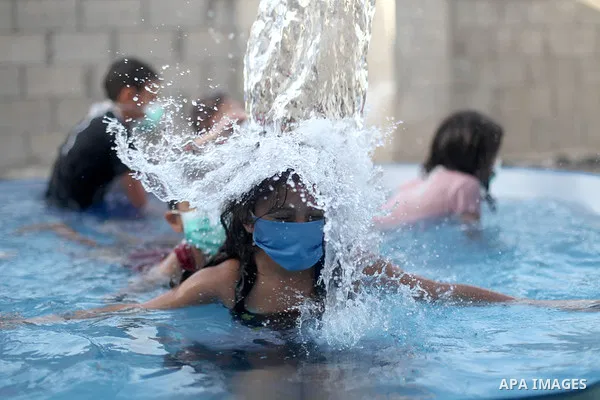Palestinian children wear face masks play together as they cool off in the water in a metal frame pool erected on the rooftop of a residential building, amid the spread of the coronavirus pandemic, in Gaza City on Septem...