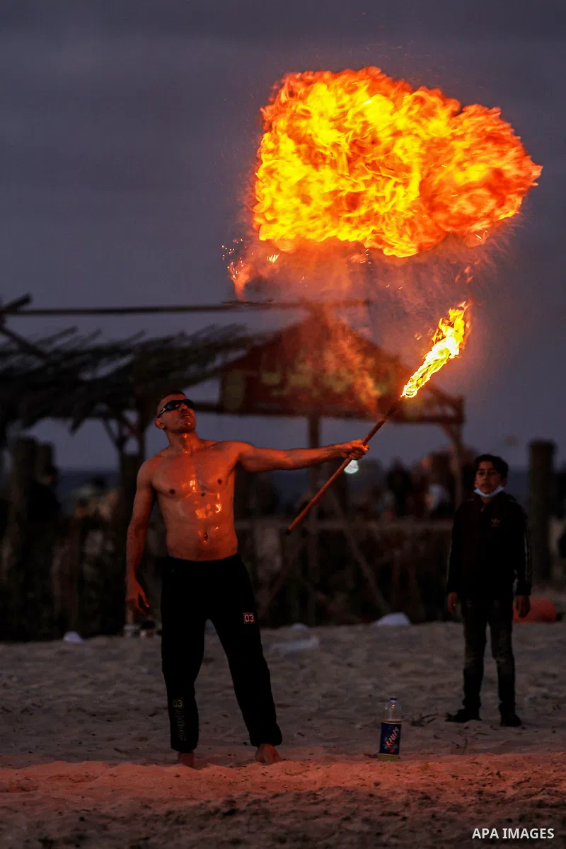 A Palestinian man performs a show with fire during sunset on the beach of the Gaza Strip on February 12, 2021. Photo by mohammed salem