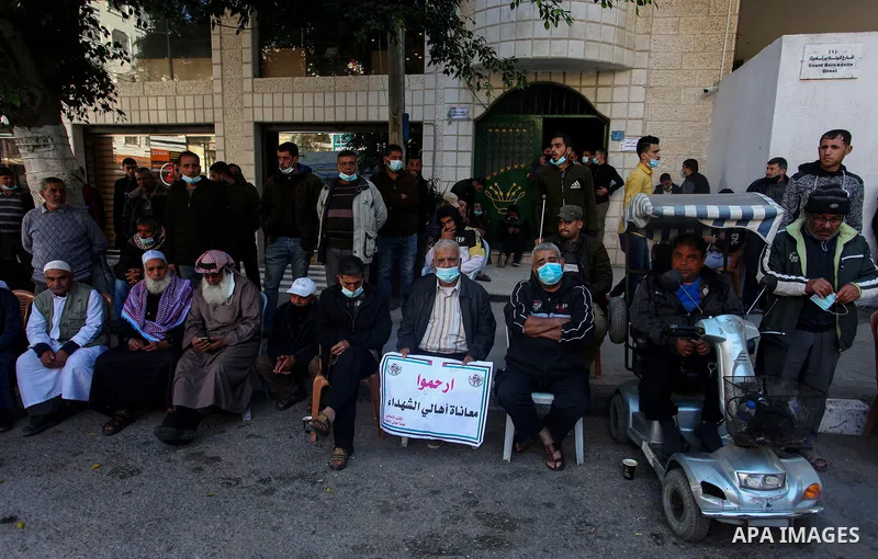 Palestinian families of martyrs and woundeds wearing protective face masks, as they take part in a protest to demand their rights and salaries, in front of the headquarters of the Martyrs and Wounded Foundation, in Gaza...