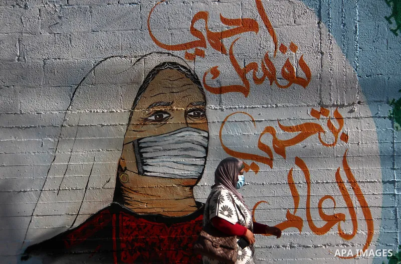 A Palestinian woman walks past a mural, in Gaza city, on February 27, 2021. Photo by Mahmoud Ajjour