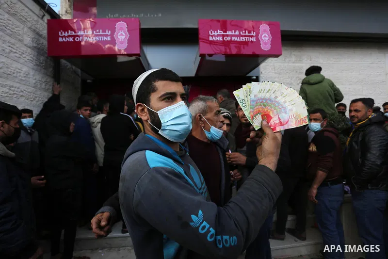Palestinian Authority employees wear face masks as they wait to receive their salaries from an ATM, outside a Palestine Bank, amid the coronavirus disease (COVID-19), in Dair Al Balah in the central of Gaza Strip, on Mar...