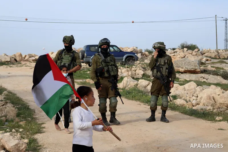 A Palestinian girl holds the Palestinian flag in front of the Israeli forces during a protest against Israeli Prime Minister Benjamin Netanyahu's visit to the heritage site of ancient Susya, in Susya village in the Israe...