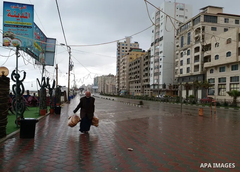 Palestinians walk in a street during a rainy day, in Gaza city, on March 26, 2021. Weather today is partly cloudy to cloudy and relatively cold to cold with a drop in temperature, which remains unseasonably low, accordin...