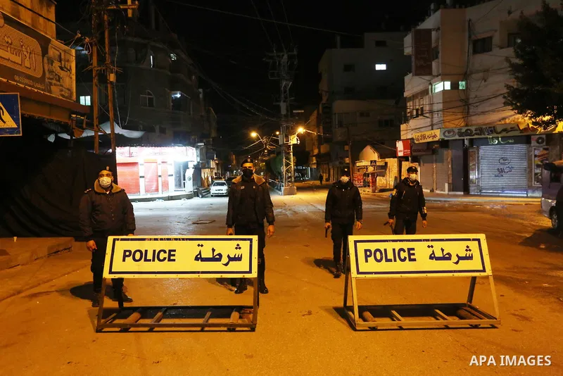 Palestinian policemen wear face masks, guard a barrier blocking a road, in Deir Al-Balah in the center of the Gaza Strip, on March 27, 2021, after the Ministry of Interior in Gaza City announced the full lockdown on Satu...