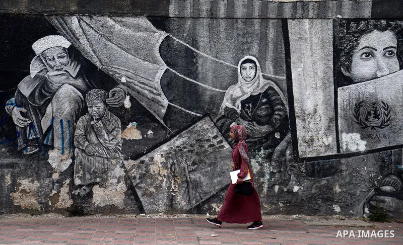 Palestinians walk past a mural, in Gaza City on April 11, 2021. The teachers in the United Nations Relief and Works Agency (UNRWA) called on the agency's management to respect the Palestinian Curricula, especially the na...
