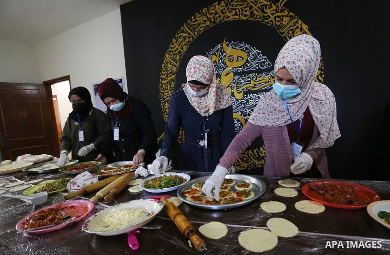 Palestinian deaf girls, wear protective and maskes prepare pastries and pizza for distribution to poor families and latecomers on the roads, during the fasting month of Ramadan, at the Hamm Association, in the Maghazi ca...