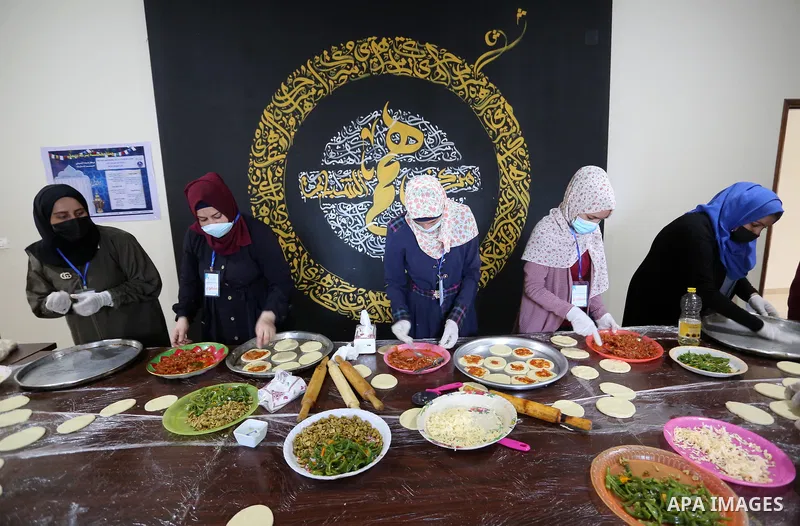 Palestinian deaf girls, wear protective and maskes prepare pastries and pizza for distribution to poor families and latecomers on the roads, during the fasting month of Ramadan, at the Hamm Association, in the Maghazi ca...
