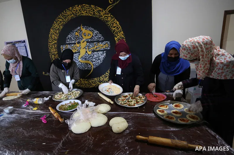 Palestinian deaf girls, wear protective and maskes prepare pastries and pizza for distribution to poor families and latecomers on the roads, during the fasting month of Ramadan, at the Hamm Association, in the Maghazi ca...