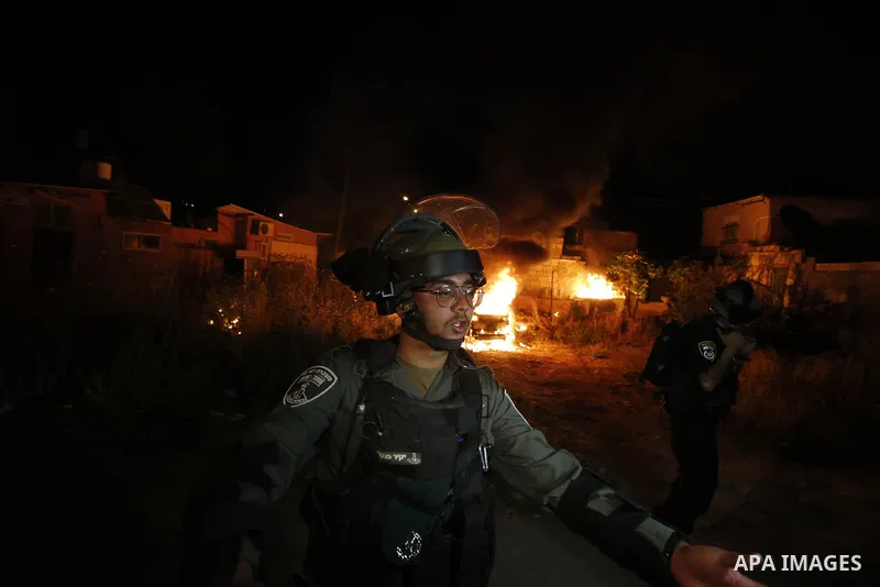 Israeli policemen gesture as a car belonging to Jewish settlers burns amid tension over the possible eviction of several Palestinian families from homes on land claimed by Jewish settlers in the Sheikh Jarrah neighbourho...