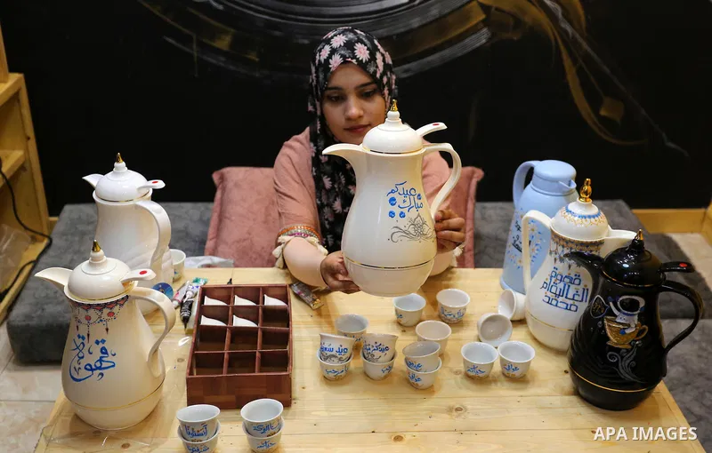 Palestinian artist, Abeer Al-Tallaa, 23, paints on the pots and cups of coffee the congratulatory phrases for Eid Al Fitr, at Maghazi refugee camp in the center of the Gaza Strip, on May 8, 2021. People flock markets and...