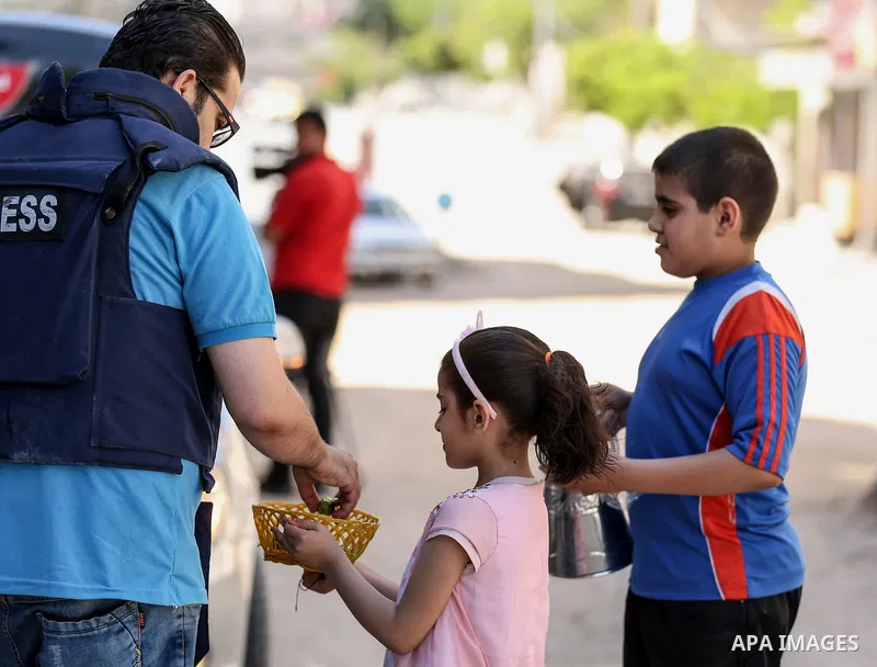 Palestinian children, Mohammad and Sarah Abbas, distribute chocolate in front of their the rubble of a building amidst Israeli air strikes, in Gaza City May 18, 2021. Heavy air strikes and rocket fire in the Israel-Gaza...