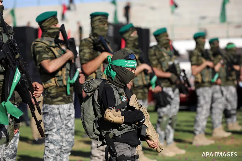 A boy stands with members of Al-Qassam Brigades, the armed wing of the Hamas movement during a rally in Gaza City on May 24, 2021. A ceasefire was reached late last week after 11 days of deadly violence between Israel an...