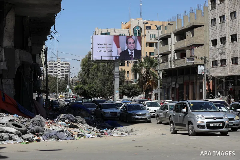 Palestinians walk past a poster of the Egyptian President Abdel Fattah el-Sisi, in Gaza city on May 30, 2021. Egypt has brokered a ceasefire agreement to end the Israeli airstrikes on the Gaza Strip, which have killed mo...