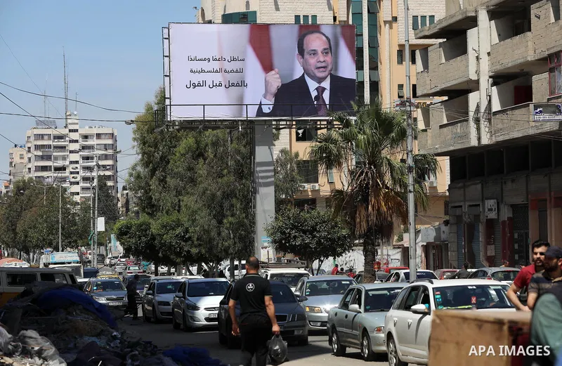 Palestinians walk past a poster of the Egyptian President Abdel Fattah el-Sisi, in Gaza city on May 30, 2021. Egypt has brokered a ceasefire agreement to end the Israeli airstrikes on the Gaza Strip, which have killed mo...