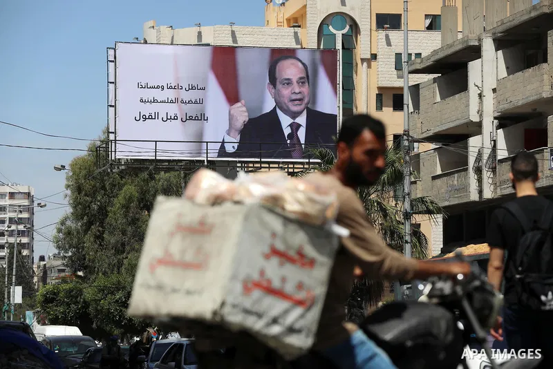 Palestinians walk past a poster of the Egyptian President Abdel Fattah el-Sisi, in Gaza city on May 30, 2021. Egypt has brokered a ceasefire agreement to end the Israeli airstrikes on the Gaza Strip, which have killed mo...