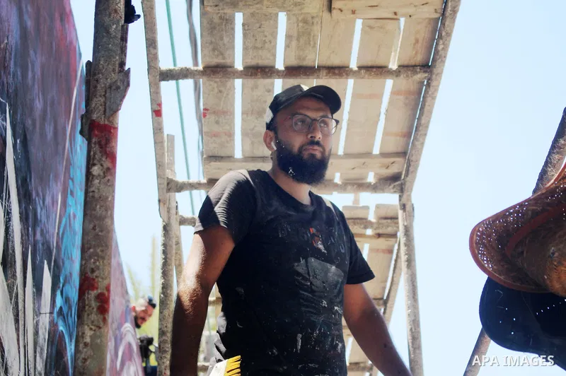 Palestinian artist Bilal Khaled draws on a wall ordinate in Gaza city on July 1, 2021. "Graffiti" (usually both singular and plural) and the rare singular form "graffito" are from the Italian word graffiato ("scratched")...