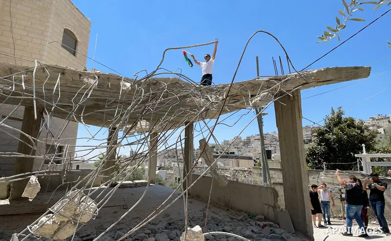 A man of Abu Ghannam family waves a Palestinian flag on the rubbles of their hous after it demolished in the East Jerusalem neighborhood of al-Tur, on July 06, 2021. Abu Ghannam family demolised thier house by thierselve...