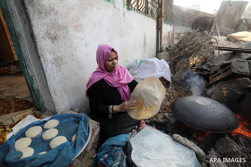 A Palestinian woman bakes a traditional bread "Taboon" ahead of Eid al-Adha festival, near rubbles of her house which was destroyed by airstrikes during an 11-day war between Hamas and Israel last May in Khan Yunis in th...