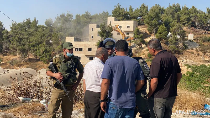 Home owners of Palestinian-built houses being demolished by Israel look on as Israeli soldiers stand by in the village of Sair northeast of Hebron on August 5, 2021, which according to Israel were built without authorisa...