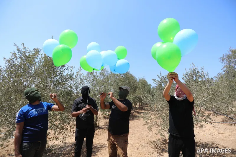 Masked Palestinians prepare incendiary balloons near Al-Bureij camp, in the center of the Gaza Strip on August 24, 2021. The Israel Forces carried out airstrikes in the Gaza Strip late Monday night in response to the lau...