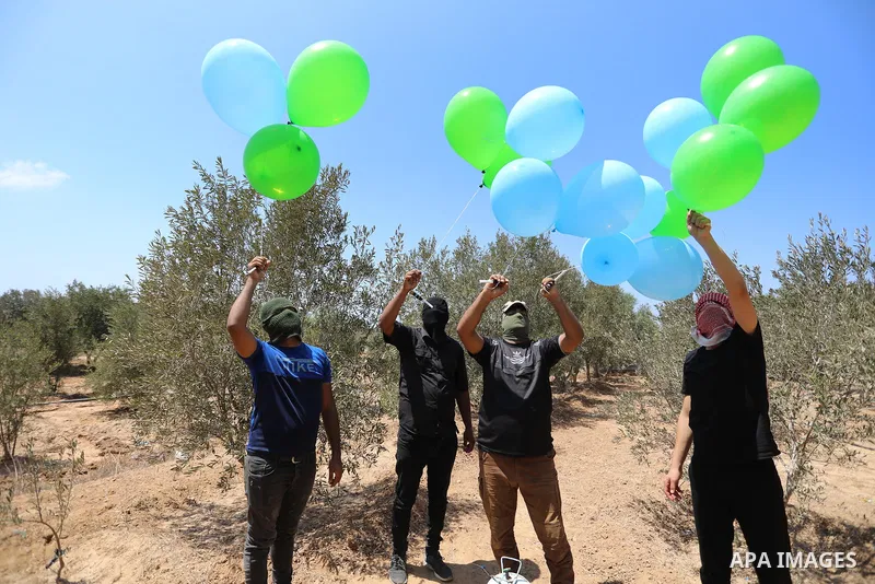 Masked Palestinians prepare incendiary balloons near Al-Bureij camp, in the center of the Gaza Strip on August 24, 2021. The Israel Forces carried out airstrikes in the Gaza Strip late Monday night in response to the lau...