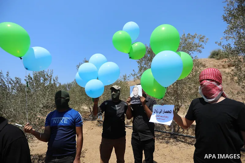 Masked Palestinians prepare incendiary balloons near Al-Bureij camp, in the center of the Gaza Strip on August 24, 2021. The Israel Forces carried out airstrikes in the Gaza Strip late Monday night in response to the lau...