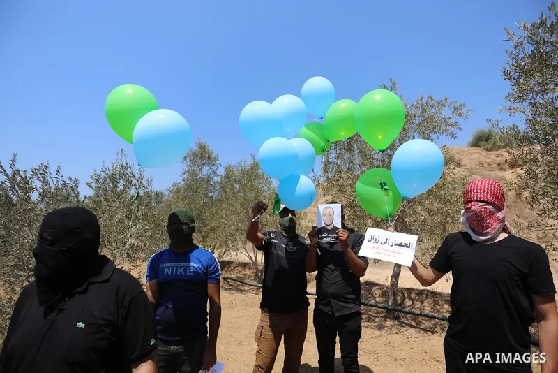 Masked Palestinians prepare incendiary balloons near Al-Bureij camp, in the center of the Gaza Strip on August 24, 2021. The Israel Forces carried out airstrikes in the Gaza Strip late Monday night in response to the lau...