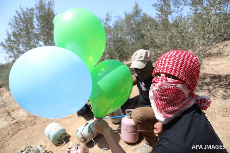 Masked Palestinians prepare incendiary balloons near Al-Bureij camp, in the center of the Gaza Strip on August 24, 2021. The Israel Forces carried out airstrikes in the Gaza Strip late Monday night in response to the lau...
