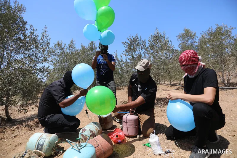 Masked Palestinians prepare incendiary balloons near Al-Bureij camp, in the center of the Gaza Strip on August 24, 2021. The Israel Forces carried out airstrikes in the Gaza Strip late Monday night in response to the lau...