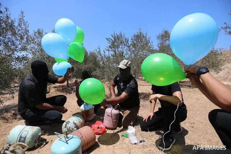 Masked Palestinians prepare incendiary balloons near Al-Bureij camp, in the center of the Gaza Strip on August 24, 2021. The Israel Forces carried out airstrikes in the Gaza Strip late Monday night in response to the lau...