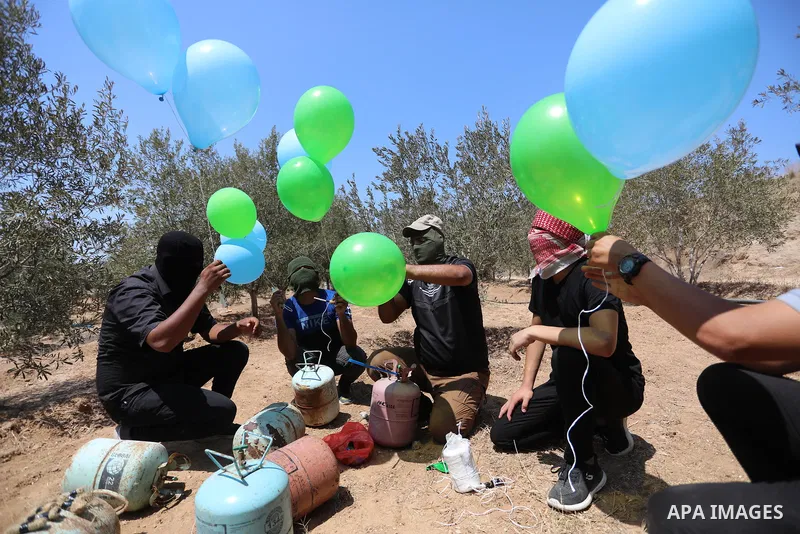 Masked Palestinians prepare incendiary balloons near Al-Bureij camp, in the center of the Gaza Strip on August 24, 2021. The Israel Forces carried out airstrikes in the Gaza Strip late Monday night in response to the lau...