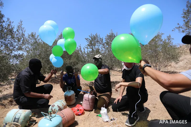 Masked Palestinians prepare incendiary balloons near Al-Bureij camp, in the center of the Gaza Strip on August 24, 2021. The Israel Forces carried out airstrikes in the Gaza Strip late Monday night in response to the lau...