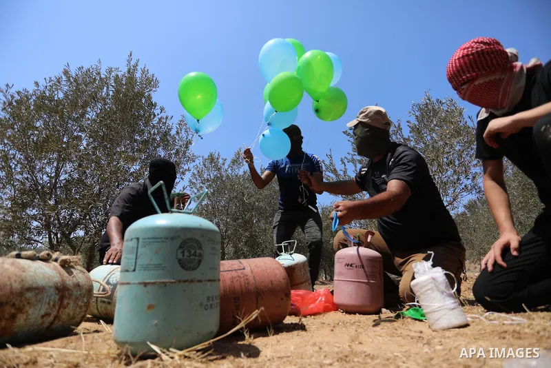 Masked Palestinians prepare incendiary balloons near Al-Bureij camp, in the center of the Gaza Strip on August 24, 2021. The Israel Forces carried out airstrikes in the Gaza Strip late Monday night in response to the lau...