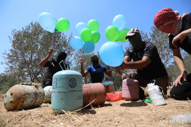 Masked Palestinians prepare incendiary balloons near Al-Bureij camp, in the center of the Gaza Strip on August 24, 2021. The Israel Forces carried out airstrikes in the Gaza Strip late Monday night in response to the lau...