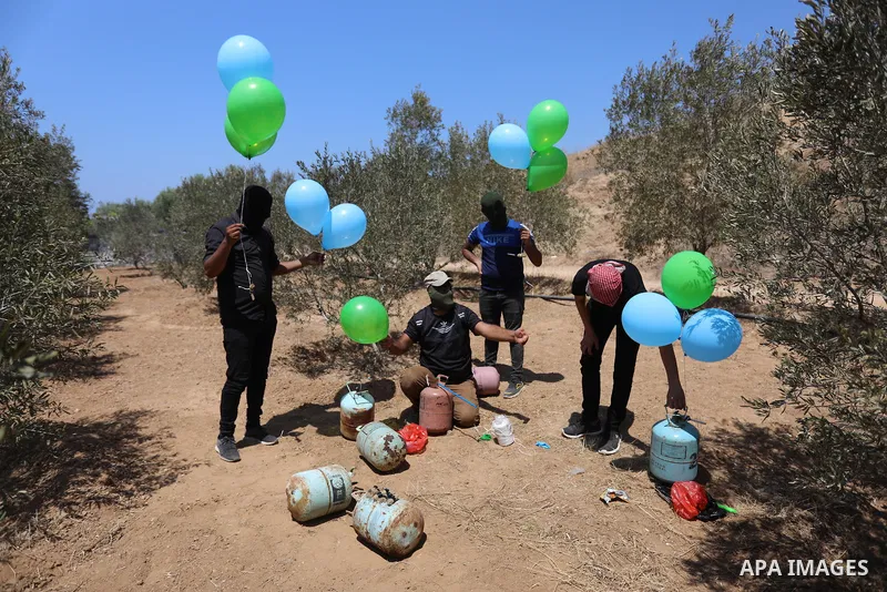 Masked Palestinians prepare incendiary balloons near Al-Bureij camp, in the center of the Gaza Strip on August 24, 2021. The Israel Forces carried out airstrikes in the Gaza Strip late Monday night in response to the lau...