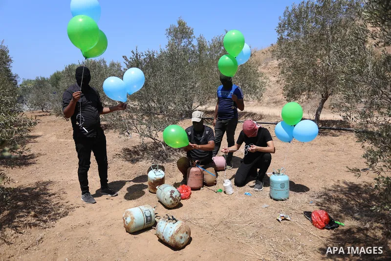 Masked Palestinians prepare incendiary balloons near Al-Bureij camp, in the center of the Gaza Strip on August 24, 2021. The Israel Forces carried out airstrikes in the Gaza Strip late Monday night in response to the lau...