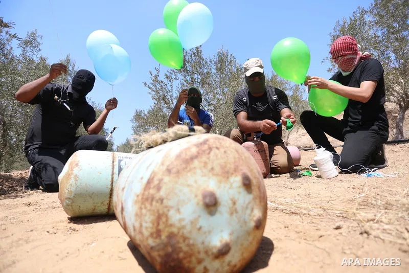 Masked Palestinians prepare incendiary balloons near Al-Bureij camp, in the center of the Gaza Strip on August 24, 2021. The Israel Forces carried out airstrikes in the Gaza Strip late Monday night in response to the lau...