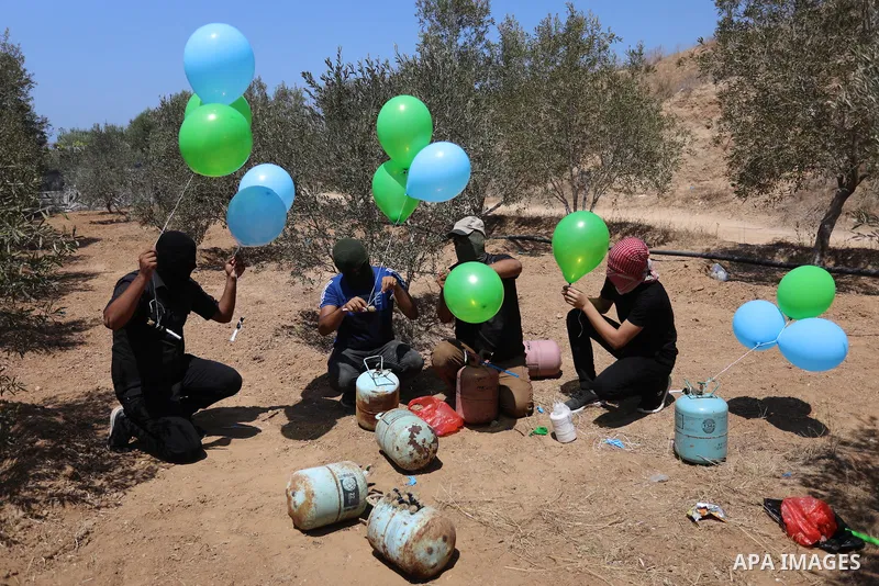 Masked Palestinians prepare incendiary balloons near Al-Bureij camp, in the center of the Gaza Strip on August 24, 2021. The Israel Forces carried out airstrikes in the Gaza Strip late Monday night in response to the lau...