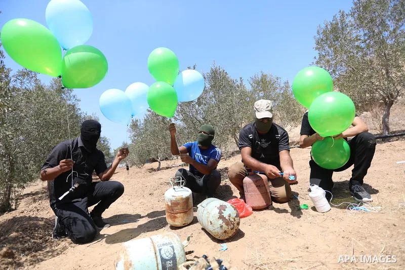 Masked Palestinians prepare incendiary balloons near Al-Bureij camp, in the center of the Gaza Strip on August 24, 2021. The Israel Forces carried out airstrikes in the Gaza Strip late Monday night in response to the lau...