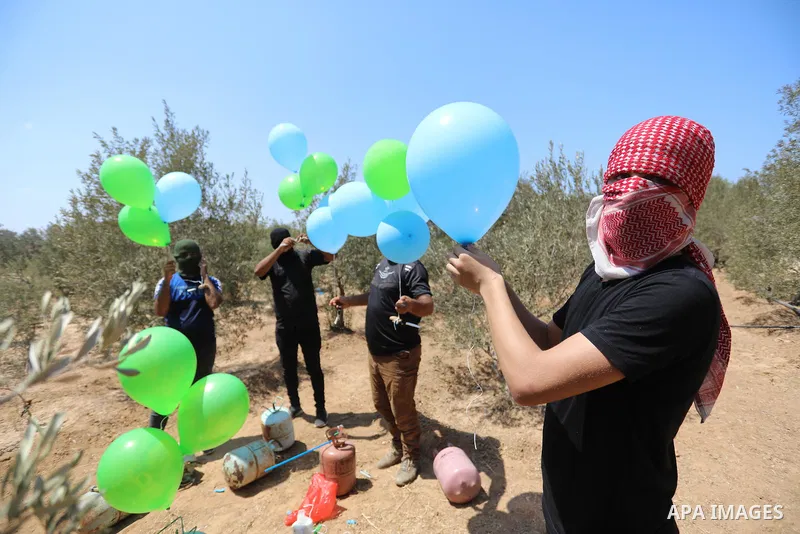 Masked Palestinians prepare incendiary balloons near Al-Bureij camp, in the center of the Gaza Strip on August 24, 2021. The Israel Forces carried out airstrikes in the Gaza Strip late Monday night in response to the lau...