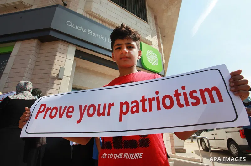Palestinian relatives of orphans and disabled hold banners during a protest against Banks policy on the closure of the accounts of charities in Gaza city on August 25, 2021. The fiscal position in Gaza strip has worsened...
