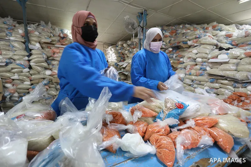 Palestinian employees at the United Nations Relief and Works Agency for Palestinian Refugees (UNRWA) wearing protective masks and gloves, prepare food aid rations for refugees, in Dair Al Balah in the center of Gaza stri...