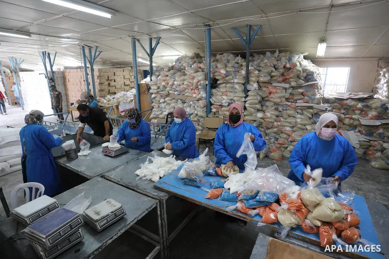 Palestinian employees at the United Nations Relief and Works Agency for Palestinian Refugees (UNRWA) wearing protective masks and gloves, prepare food aid rations for refugees, in Dair Al Balah in the center of Gaza stri...