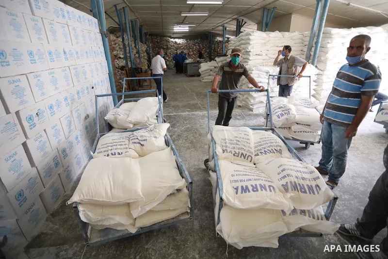Palestinian employees at the United Nations Relief and Works Agency for Palestinian Refugees (UNRWA) wearing protective masks and gloves, prepare food aid rations for refugees, in Dair Al Balah in the center of Gaza stri...