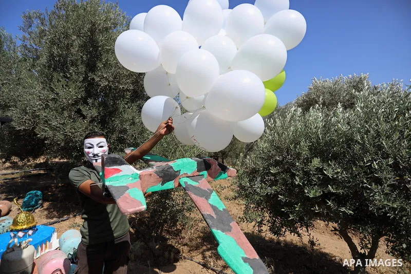 Masked Palestinians prepare incendiary balloons near Jabalia in the northern of Gaza Strip, on September 4, 2021. Reports in Palestinian media indicated that units in charge of incendiary balloon attacks on Israeli plann...
