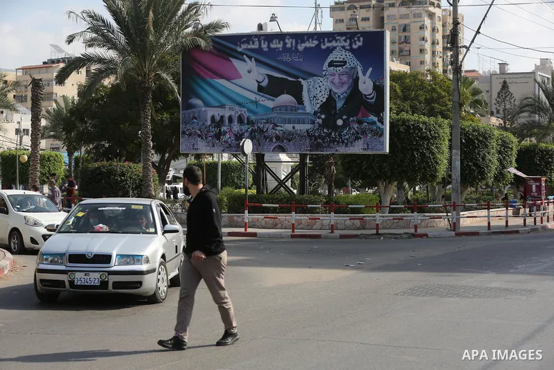 Palestinians walk past a photo depicting late president Yasser Arafat to mark the 17th anniversary of his death, in Gaza city on November 11, 2021. Photo by Ashraf Amra