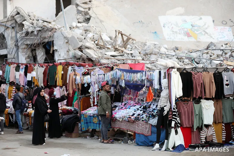 Palestinian street vendors sell clothes near the rubble of al-Shuruq tower in Gaza City's al-Rimal neighbourhood which was targeted by Israeli strikes during the recent confrontations between Hamas and Israel, on Novembe...